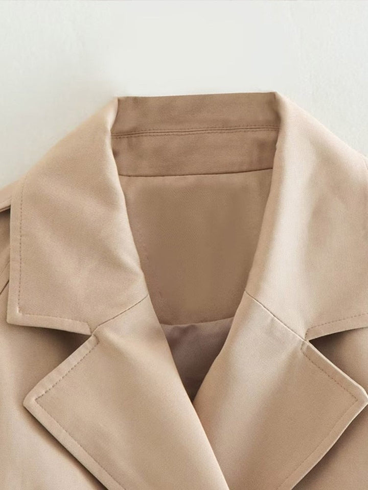 "Cropped beige trenchcoat voor dames, stijlvolle dubbele rij knopen en verstelbare manchetten, elegant en modern ontwerp."