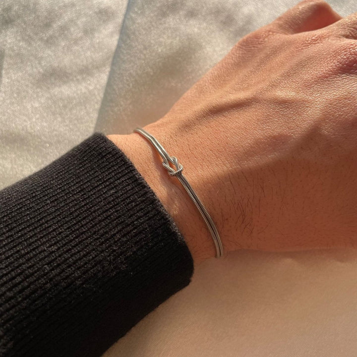 "Elegant damesarmband met liefdesknoopdesign, verstelbaar, minimalistisch en stijlvol in goud of zilverkleur."