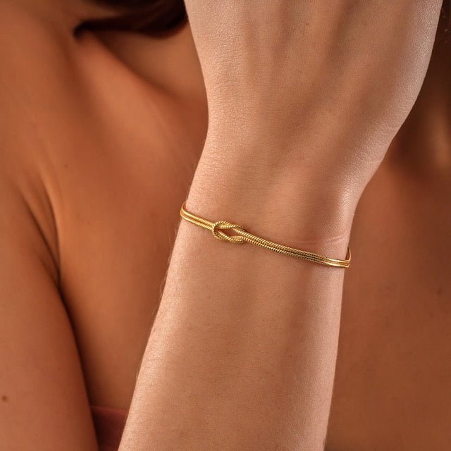"Elegant damesarmband met liefdesknoopdesign, verstelbaar, minimalistisch en stijlvol in goud of zilverkleur."