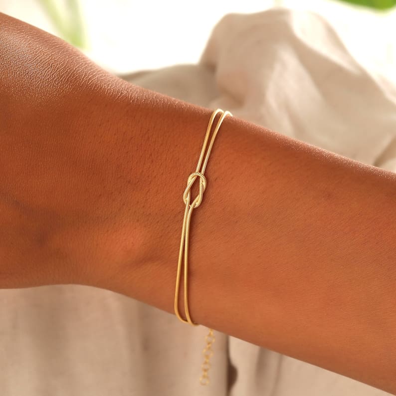 "Elegant damesarmband met liefdesknoopdesign, verstelbaar, minimalistisch en stijlvol in goud of zilverkleur."