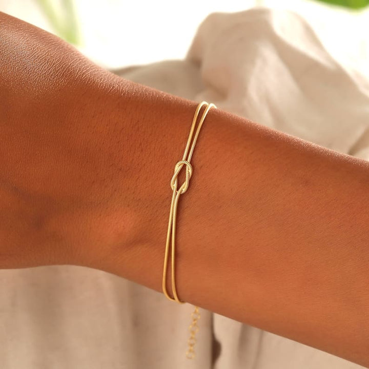 "Elegant damesarmband met liefdesknoopdesign, verstelbaar, minimalistisch en stijlvol in goud of zilverkleur."