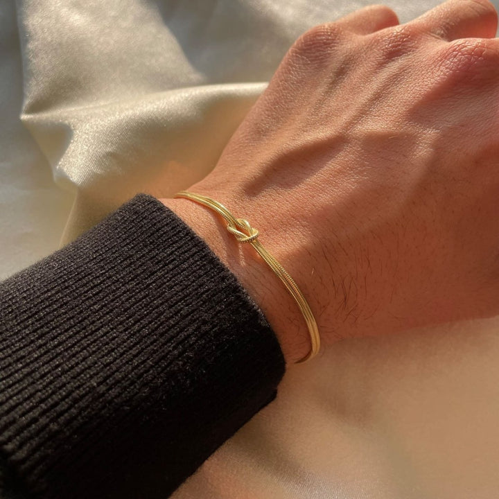 "Elegant damesarmband met liefdesknoopdesign, verstelbaar, minimalistisch en stijlvol in goud of zilverkleur."