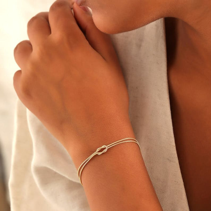 "Elegant damesarmband met liefdesknoopdesign, verstelbaar, minimalistisch en stijlvol in goud of zilverkleur."