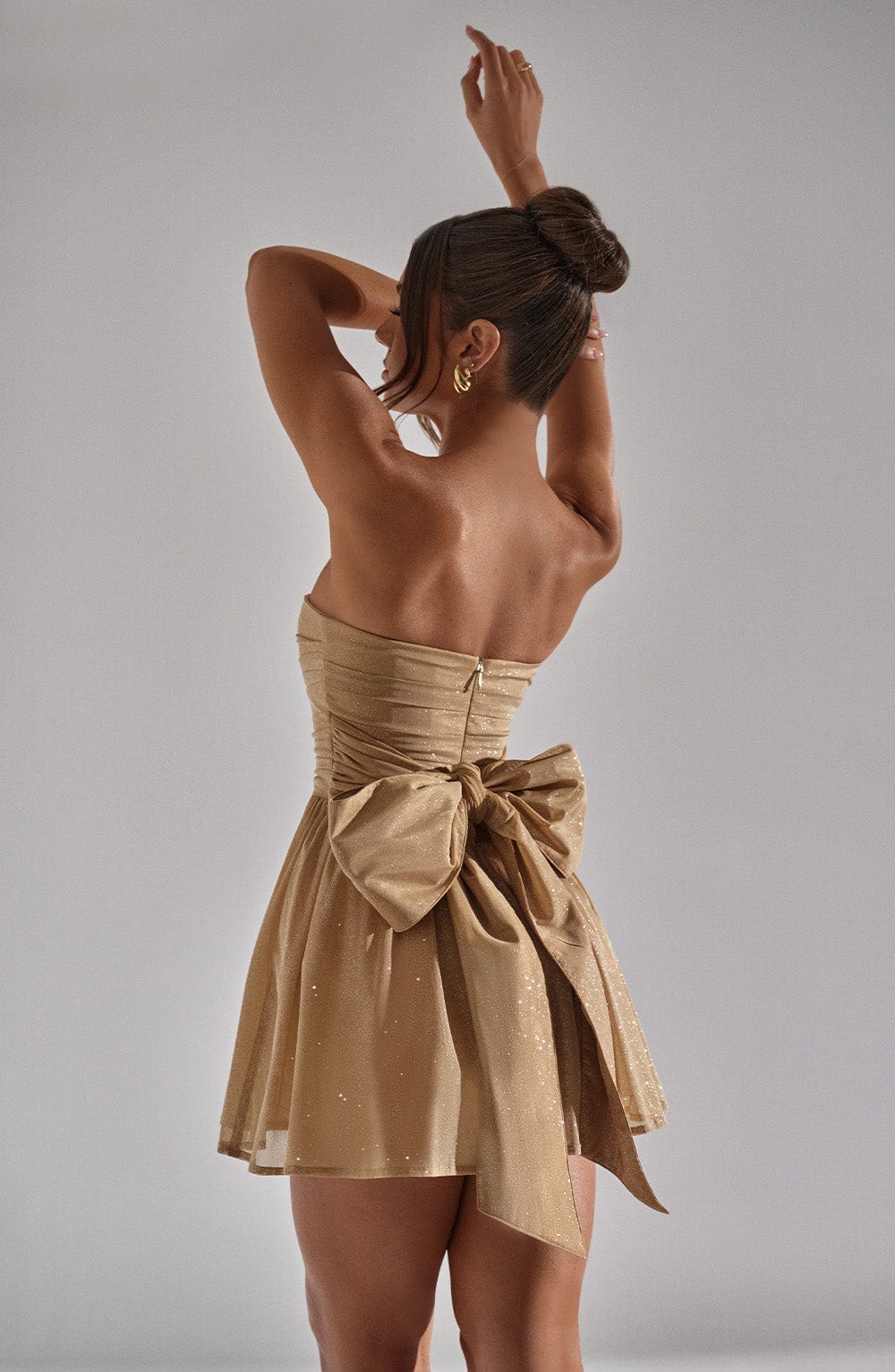 "Glimmende strapless mini-jurk met gouden glitters, flared rok en oversized strik - perfecte partyjurk voor dames."