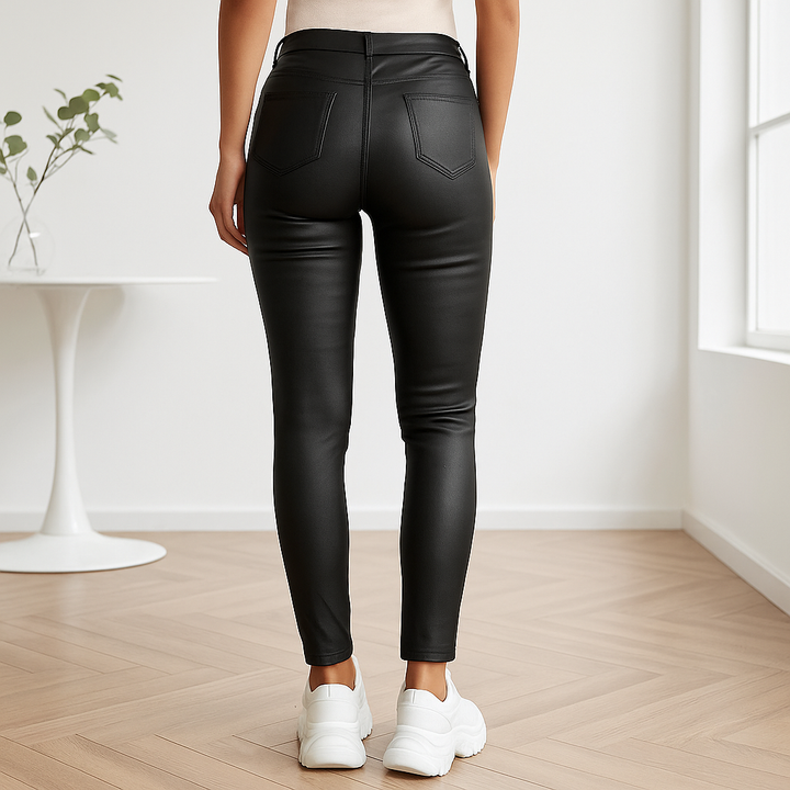 Vrouw draagt zwarte, stretchy skinny imitatieleren broek met hoge taille en witte sneakers, vooraanzicht.